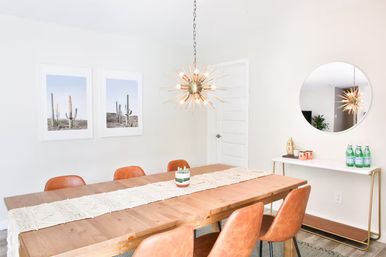 Bright modern dining room with long wooden table, macramé runner, six tan leather chairs, spiky sputnik chandelier, round wall mirror and cactus wall art