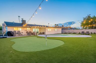 Evening suburban backyard with artificial putting green, kidney-shaped pool, patio seating and twinkling string lights