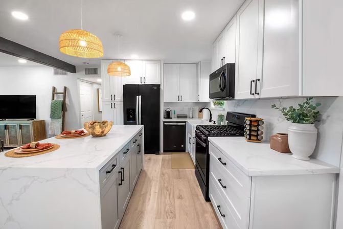 Bright modern kitchen with white shaker cabinets, large marble-look island with place settings, black stainless appliances, woven pendant lights, light hardwood floors and minimalist decor