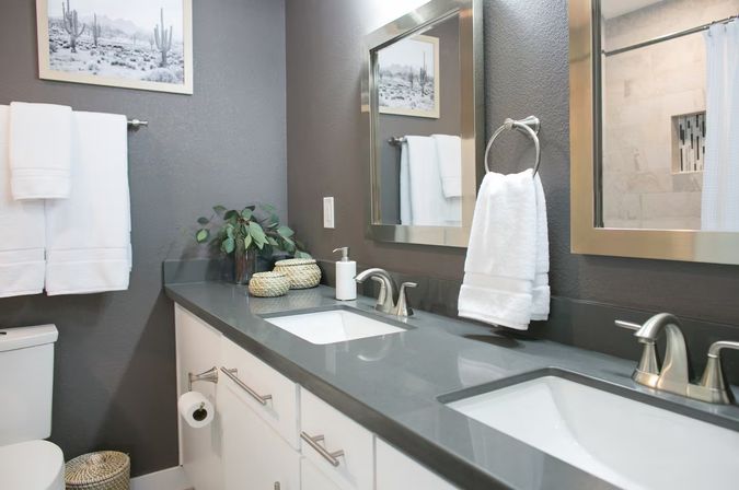 Contemporary home bathroom with double vanity, gray quartz countertop, undermount sinks, brushed nickel faucets, framed mirrors, white towels and a small decorative plant.