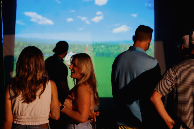 Group of friends laughing and watching a large projected virtual golf course at an indoor golf simulator