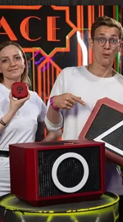 Four people in white shirts pose with red geometric game props showing a circle and triangle on a neon-lit indoor game-room set.