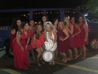 Bride-to-be in a white sash and veil posing with a group of women in red dresses in a nighttime parking lot in front of a blue van — playful bachelorette party photo.