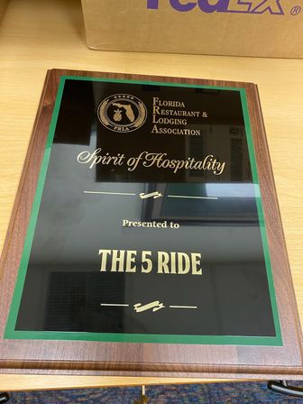 Wood-framed Florida award plaque reading “Spirit of Hospitality” from the Florida Restaurant & Lodging Association, laid on a light wood desk