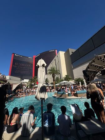 Las Vegas daytime pool party at a crowded resort pool with cabanas, palm trees and high-rise towers under a clear blue sky