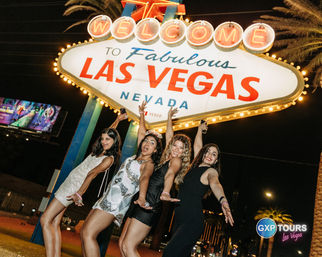 Group of four women posing and cheering at night beneath the illuminated "Welcome to Fabulous Las Vegas Nevada" sign