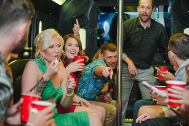Friends partying inside a lit party bus, laughing and holding red cups around a center pole — lively nightlife celebration on the go