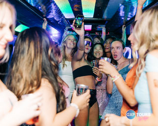 Group of young women partying inside a LED-lit party bus in Las Vegas, laughing, holding drinks and taking a selfie during a bachelorette-style night out.