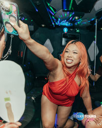 Smiling woman with orange hair in a red dress reaching to take a selfie inside a disco-lit party limo