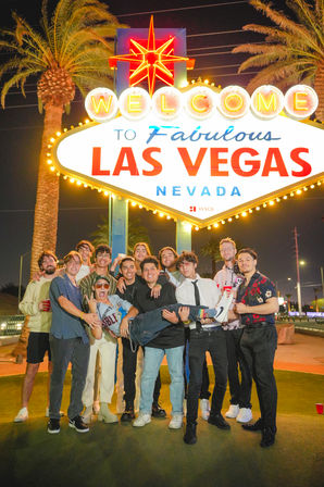 Playful group of friends posing at night under the iconic "Welcome to Fabulous Las Vegas, Nevada" sign with neon lights and palm trees in the background.