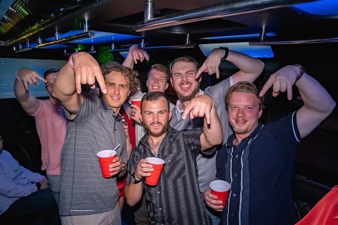Group of men laughing and posing with red cups inside a colorful party bus, energetic nightlife celebration.