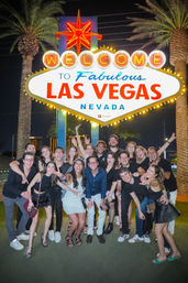Group of smiling friends posing at night beneath the iconic Welcome to Fabulous Las Vegas Nevada sign with palm trees