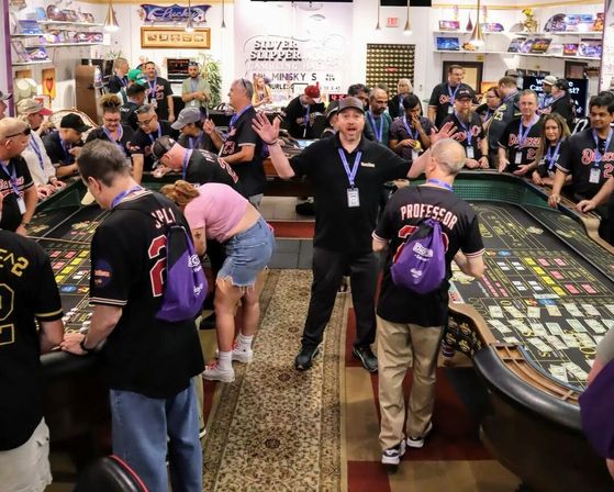 Crowded casino gaming event around large craps tables with players and dealers, a man in the center raising his arms while others place bets and cheer.