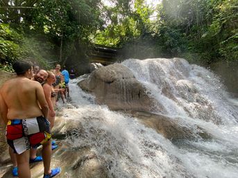 Group of people in swimsuits climbing a multi-tier tropical waterfall over smooth limestone cascades surrounded by lush green jungle