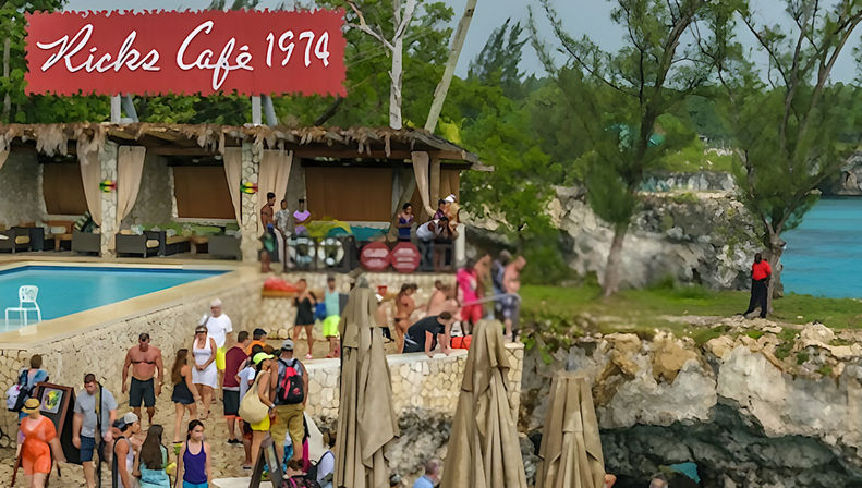Busy tropical cliffside cafe and pool with cabanas and closed umbrellas, crowds in swimwear on limestone ledges overlooking turquoise ocean