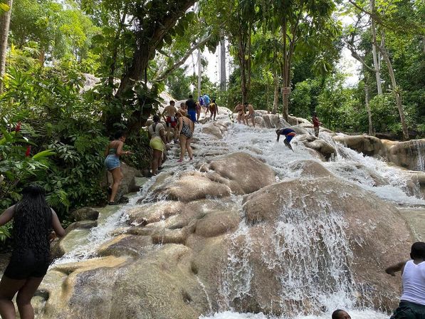 Visitors climbing a terraced tropical waterfall over smooth limestone rocks, cascading water flowing amid dense green jungle foliage.
