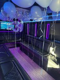 Party bus interior decorated for a 31st birthday with white and clear helium balloons, iridescent silver '31' foil numbers, purple-blue LED accent lighting and black leather bench seating.