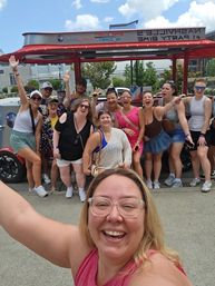 Large group of friends taking a cheerful group selfie in front of a red Nashville party bike on a sunny day