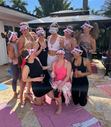 Sunny backyard bachelorette party on a palm-lined patio — bride in white and her squad wearing 'SQUAD' visors, laughing and toasting with champagne.