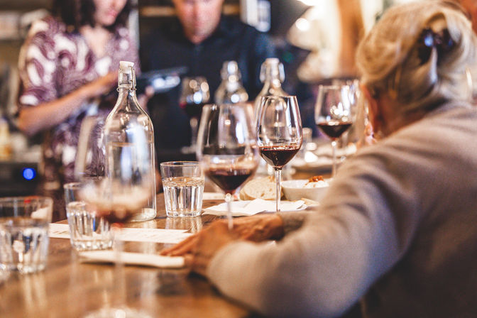 Group wine tasting at a cozy tasting room with red wine glasses, water carafe and bread on a wooden bar