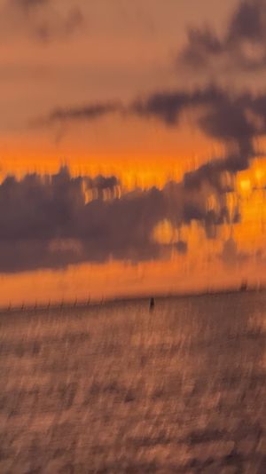 Dreamy motion-blurred orange sunset over the ocean, dark cloud silhouettes on the horizon and shimmering reflections across the water.