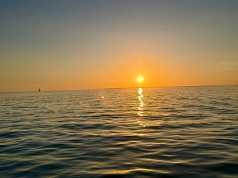 Golden sunset over calm ocean with the sun reflecting in a shimmering trail on rippling water and a lone sailboat on the distant horizon.