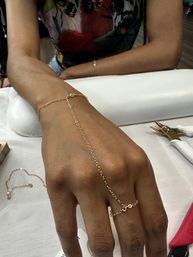 Delicate gold hand chain linking a ring to a wrist bracelet on a person’s hand resting on a salon table with manicure tools nearby.