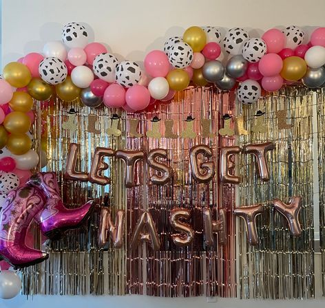 Cowgirl birthday party backdrop with pink, gold and cow-print balloon garland, metallic fringe curtain, rose-gold letter balloons and pink cowboy-boot foil balloons.