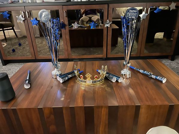 Festive blue-and-silver 35th birthday setup on a wooden coffee table: gold crown, party horns, star foil centerpieces and a mirrored cabinet in the background.