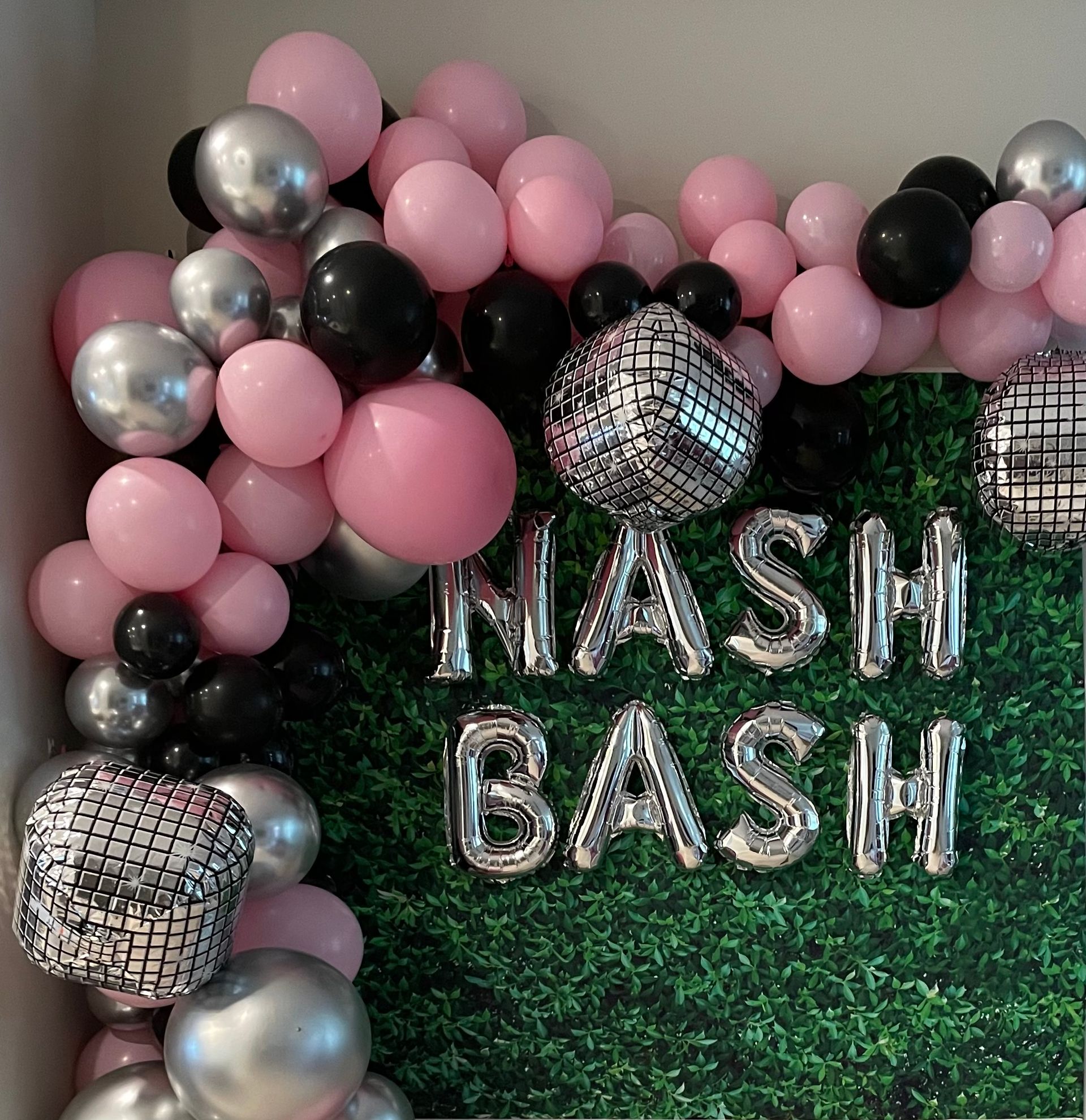 Festive pink, black, and silver balloon garland framing a faux boxwood party backdrop with mirrored disco-cube balloons and silver letter balloons spelling NASH BASH.