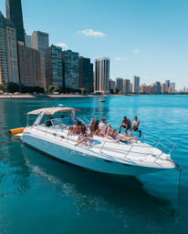 Group of people sunbathing and hanging out on a white yacht on turquoise lake water with a high-rise urban waterfront skyline and clear blue summer sky
