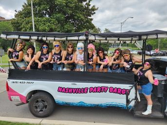 Group of women in retro wigs and matching 'Let's Go' tanks posing on an open-air party vehicle in Nashville, wearing mirrored sunglasses and denim shorts