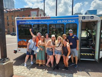 Group of adults smiling and posing in front of a blue sightseeing tour bus in downtown Nashville on a sunny day