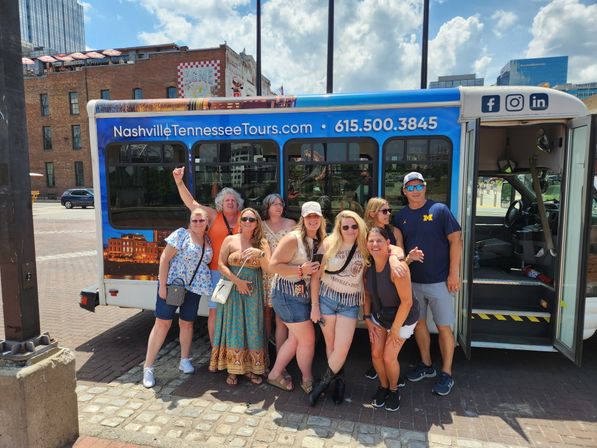Group of adults smiling and posing in front of a blue sightseeing tour bus in downtown Nashville on a sunny day
