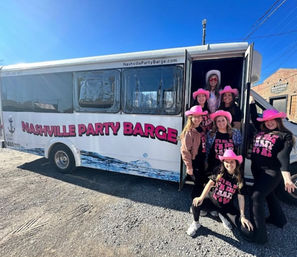 Group of women in pink cowboy hats posing by a white Nashville party shuttle with bright pink lettering on a sunny day