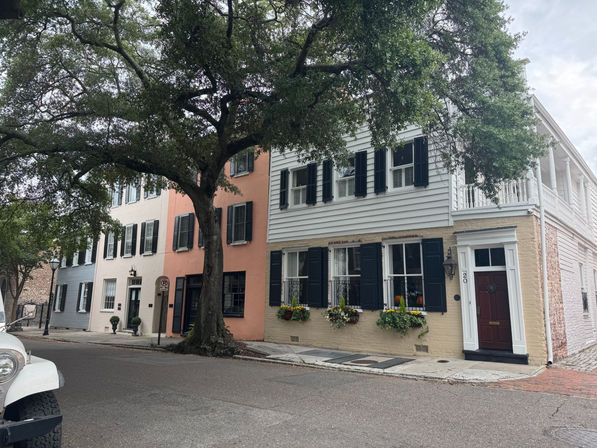 Charming historic rowhouses with black shutters and window flower boxes, peach and white facades, and a large oak shading a quiet corner street