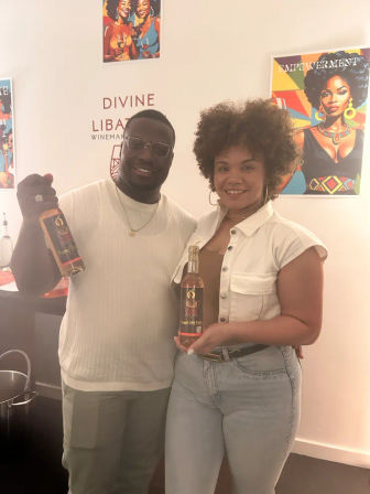 Two smiling people holding bottles of rosé wine in a bright indoor wine-tasting room with colorful, empowering artwork on the walls.