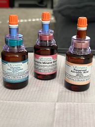 Three amber vitamin infusion bottles with colorful ports and orange caps on a white clinic tray — IV therapy supplies for vitamin and mineral injections.