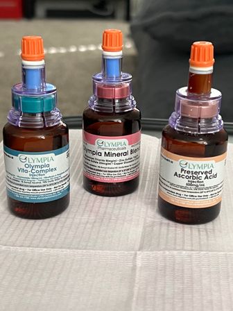 Three amber vitamin infusion bottles with colorful ports and orange caps on a white clinic tray — IV therapy supplies for vitamin and mineral injections.