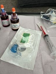 Clinic treatment tray on a disposable drape with sealed sterile dressing and tubing, two amber reagent bottles with orange caps, and a 10 mL syringe ready for use.