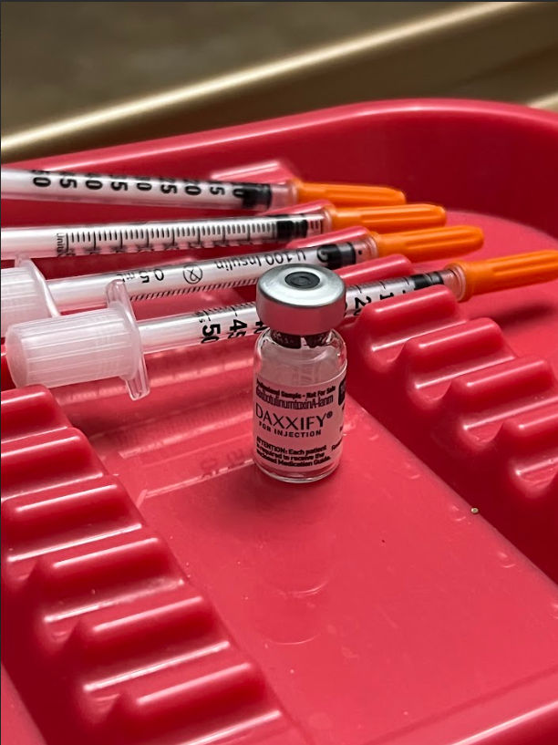 Cosmetic injectable vial and three syringes with orange caps on a red medical tray in a clinic setting