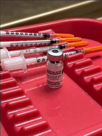 Cosmetic injectable vial and three syringes with orange caps on a red medical tray in a clinic setting