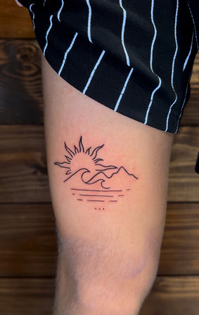 Minimal black line tattoo on inner forearm: stylized sun rising over ocean waves and mountains with reflective lines below, close-up photo with striped shorts visible