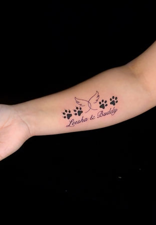 Forearm tattoo showing a delicate dove outline above a row of black dog paw prints and cursive names — a minimal black-ink pet tribute.