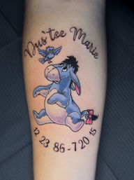 Colorful forearm tattoo of Eeyore (Winnie the Pooh) with a small bluebird above and pink tail bow, framed by cursive name script and a semi-circle of black numbers.