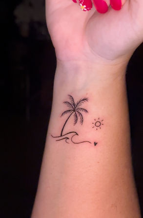 Minimalist wrist tattoo of a tiny palm tree on a small island with waves, sun, and a little heart — beach-inspired tropical design on inner wrist.