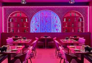 Vibrant pink restaurant interior with neon-lit arched shelves displaying bottles, a glowing blue central art panel, and neatly set tables and chairs