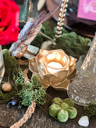 Gold lotus votive candle centerpiece on a moss-covered table with a red rose, bundled sage, decorative glass vase and crystal accent — rustic indoor table decor