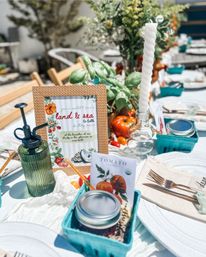 Bright al fresco farm-to-table table setting with ripe tomatoes and basil, twisted white taper candle, framed land & sea sign, mason jar and teal berry baskets for a sunny garden brunch.