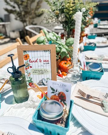 Bright al fresco farm-to-table table setting with ripe tomatoes and basil, twisted white taper candle, framed land & sea sign, mason jar and teal berry baskets for a sunny garden brunch.